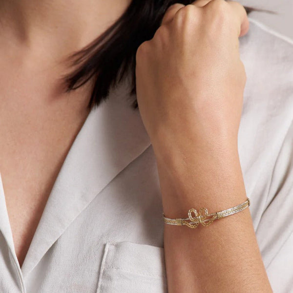 Gold bow bracelet on a person's wrist with a neutral background