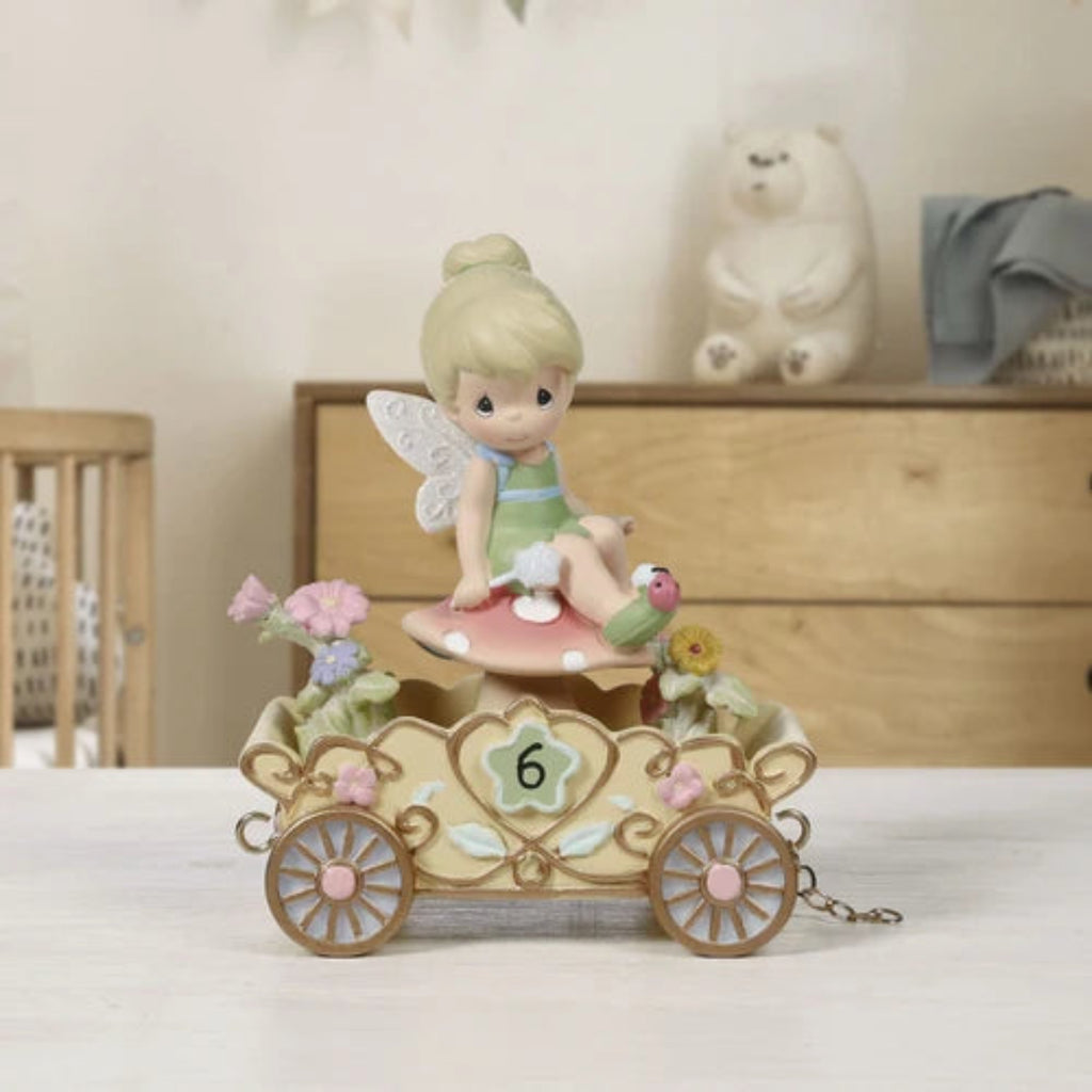 Decorative figurine of a fairy on a pink mushroom with flowers and a lady bug on her shoe.  All in a carriage, placed on a surface.