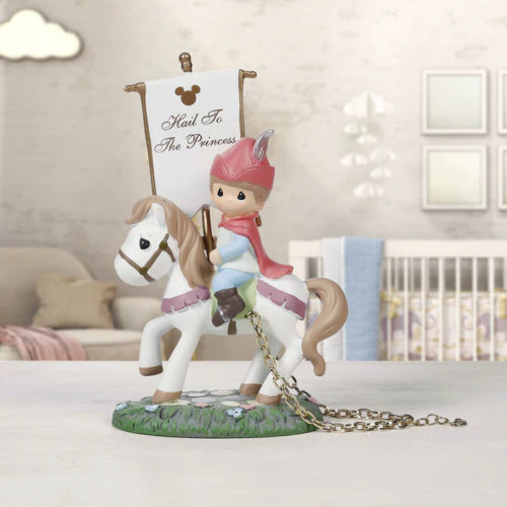 A Precious Moments style figurine of a princess in a pink hat and cape riding a white horse, holding a banner that reads 'Mail To The Princess' with a Mickey Mouse icon. The figurine is displayed on a tabletop with a softly blurred nursery background.