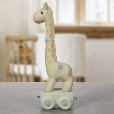A ceramic giraffe toy on a small wheeled base, standing on a gray tabletop with a softly blurred nursery background.