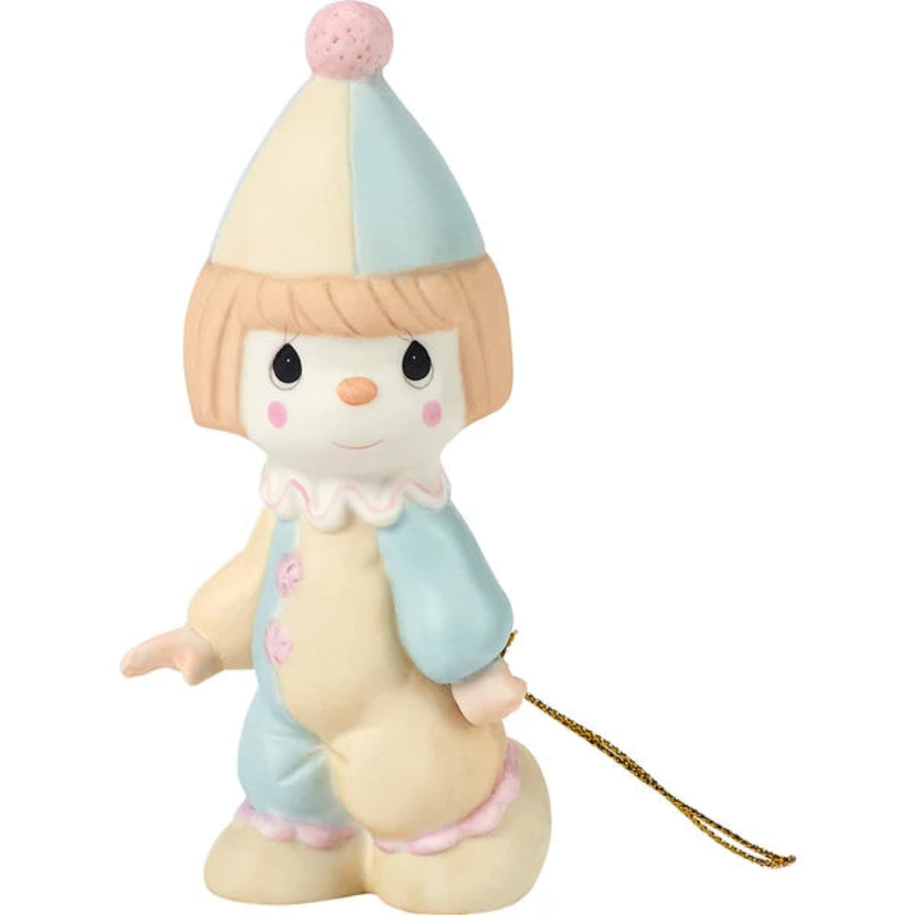 A ceramic figurine of a cute, stylized child character wearing a pastel blue and cream pointed hat with a pink pom-pom, a cream jumpsuit with pink accents, and holding a gold-colored string.