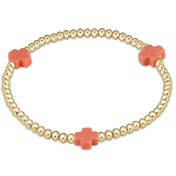Gold beaded bracelet with 3 coral crosses on a white background
