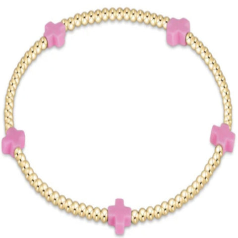 Gold bracelet with small beads and bright pink crosses on a white background