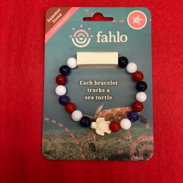 A fahlo brand beaded bracelet displayed on its retail backing card, set against a solid red background. The bracelet features red, white, and dark blue beads with a white turtle charm.