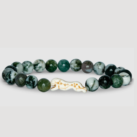 Green beaded bracelet with a ivory and gold charm on a light gray background