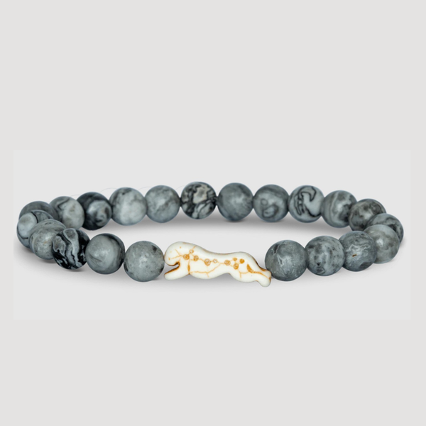 Gray beaded bracelet with a gold and ivory charm on a light gray background