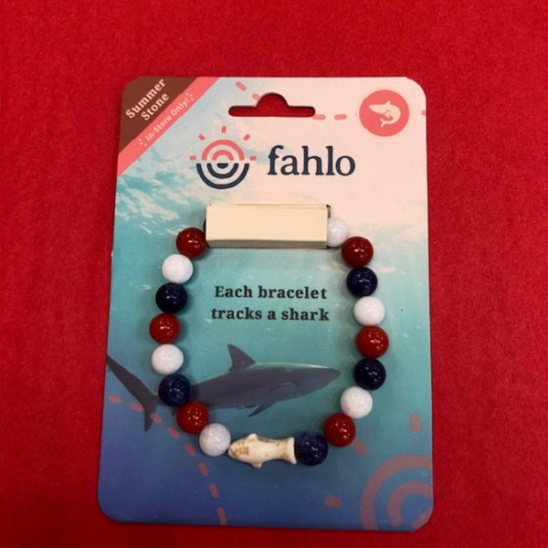 A Fahlo brand shark-themed bead bracelet on its original retail backing card, displayed against a solid red background. The bracelet features red, white, and navy blue beads with a small white fish charm.