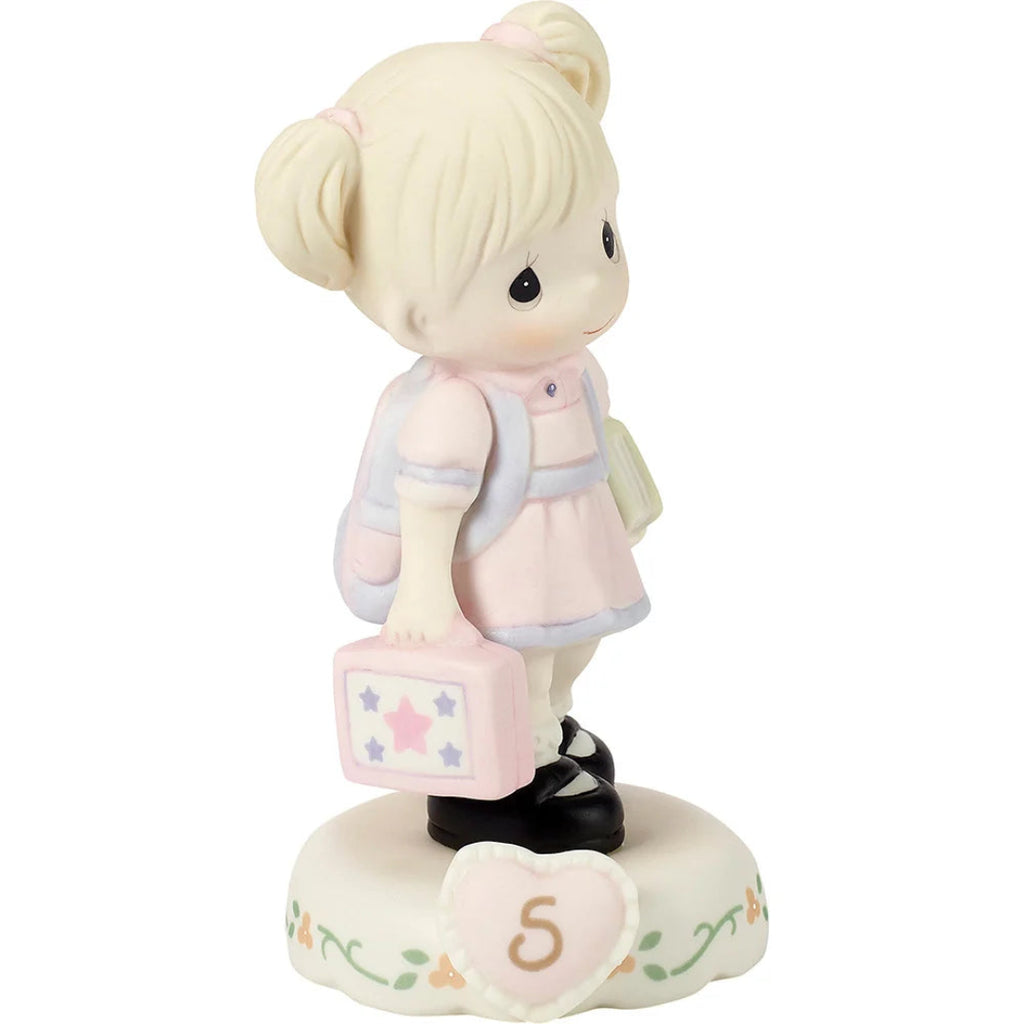 A Precious Moments figurine of a young girl with blonde pigtails, wearing a pink and blue dress and carrying a pink suitcase, standing on a decorated base with the number 5.