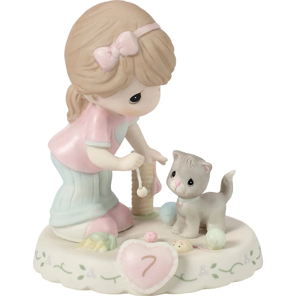 A Precious Moments figurine depicting a young girl with blonde hair and a pink bow kneeling beside a small gray kitten on a decorated base.