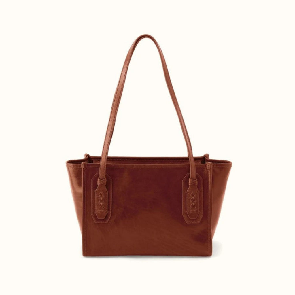 A brown leather tote bag with dual shoulder straps and decorative strap tabs, shown against a plain off-white background.