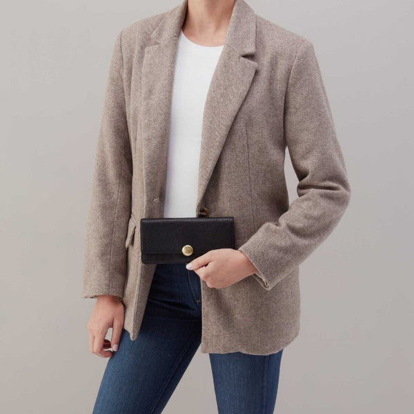 A model wearing a light taupe wool-blend blazer over a white top and blue jeans, holding a black leather clutch with a gold button.
