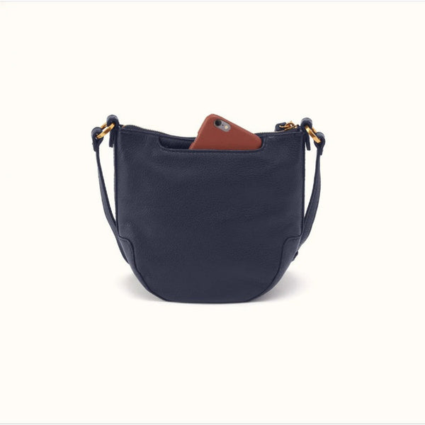A navy blue pebbled leather crescent-shaped shoulder bag with gold-tone hardware, shown on a clean off-white background with a brown phone partially tucked into its top pocket.