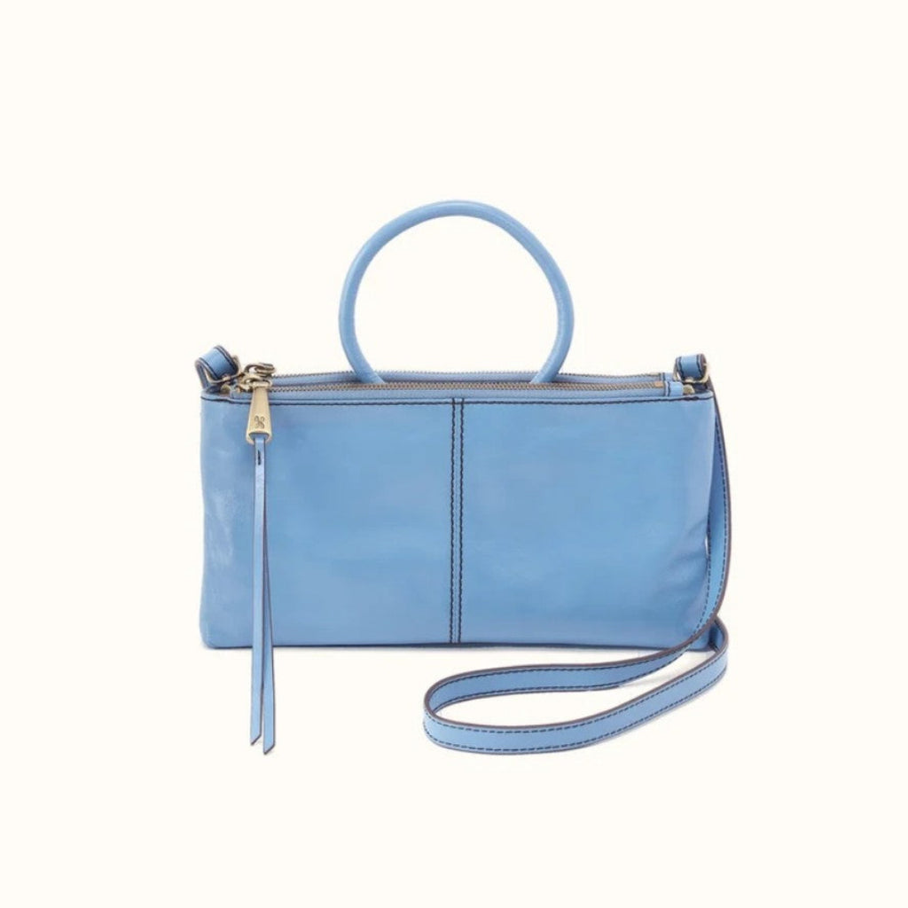 A light blue leather handbag with a top handle, a long shoulder strap, and a zipper closure, shown against a plain off-white background.
