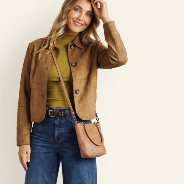 A woman models a cropped brown suede jacket over an olive green top, paired with blue jeans and a matching brown crossbody bag, against a plain off-white background.