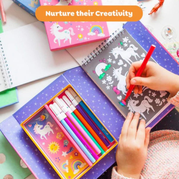 Child drawing with colored pencils on a unicorn-themed coloring book, surrounded by art supplies.