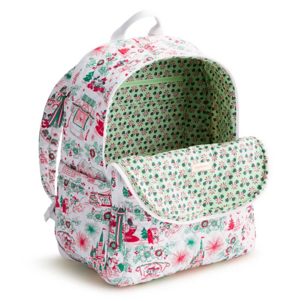 A white backpack featuring a festive Christmas-themed print with red and green illustrations of trees, snowflakes, gingerbread houses, and carousel scenes, shown against a plain white background.
