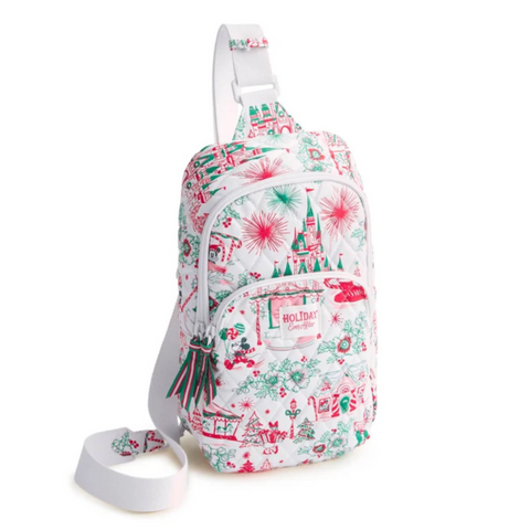 A white sling backpack with a festive Christmas print featuring red and green illustrations of houses, candy canes, fireworks, and ornaments. It has a front zippered pocket with a 'Holiday Collection' patch, a tassel charm, and an adjustable shoulder strap, shown on a plain white background.