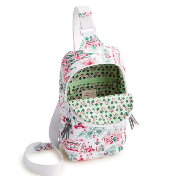 A small shoulder bag with a white base and a festive Christmas village print in red, green, and blue. The bag features a white adjustable shoulder strap, a zippered main compartment, and a front zippered pocket.