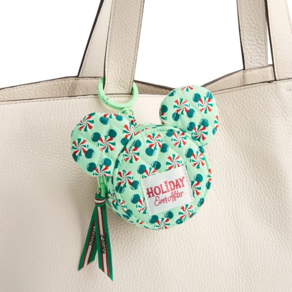A mint green Mickey Mouse-shaped holiday coin purse with a candy cane pattern, hanging from a cream-colored leather tote bag. The coin purse features a white patch with red text reading 'HOLIDAY Ever After' and has green and red tassels.