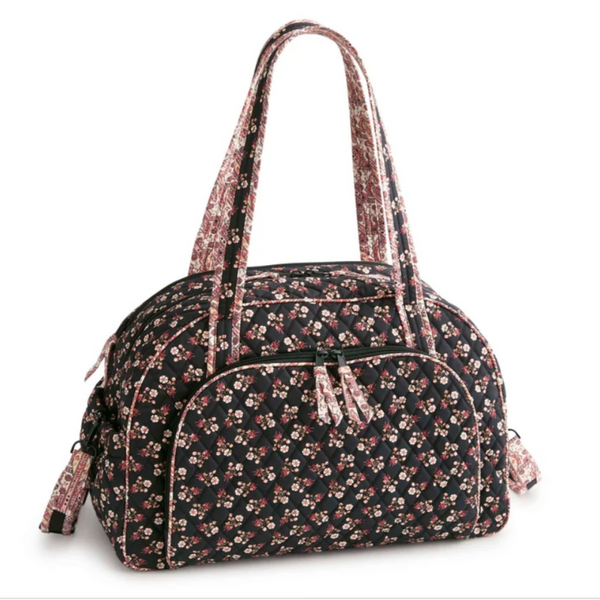 A floral print duffel bag with a black background, featuring small pink, red, and white flowers. It has dual top handles, a front zippered pocket, and a matching shoulder strap, shown on a plain white background.