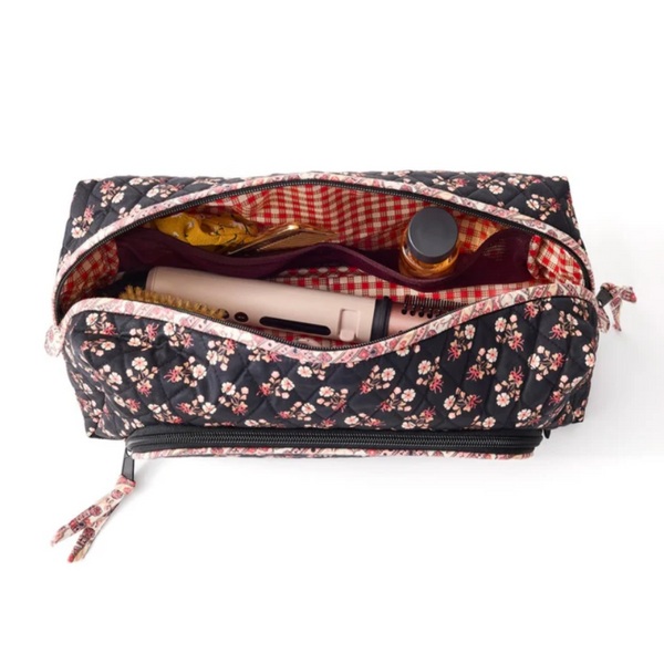 A quilted rectangular makeup bag with a black floral print exterior and a red-and-white checkered lining, shown open with cosmetics inside on a white background.