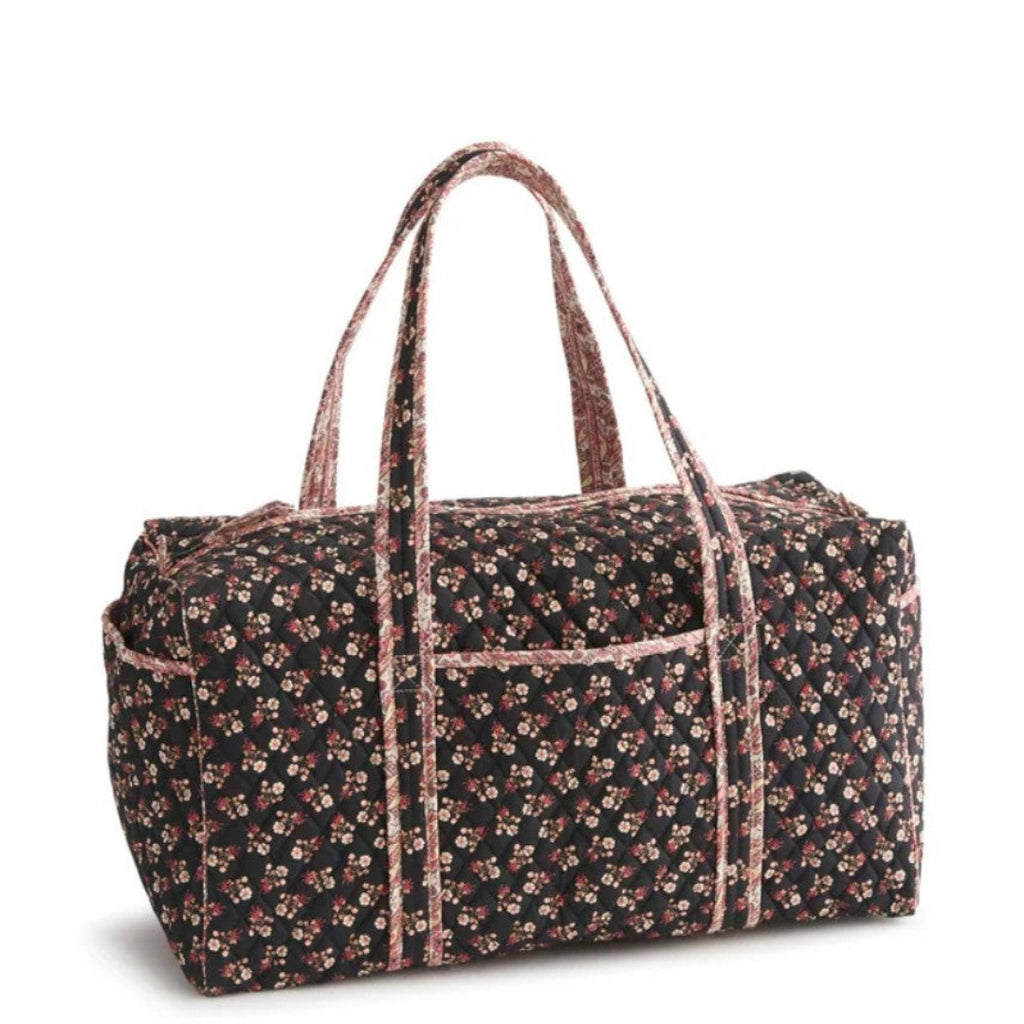 A duffel bag with a black background covered in a small pink and white floral print, featuring dual shoulder straps and a front pocket, shown on a white background.