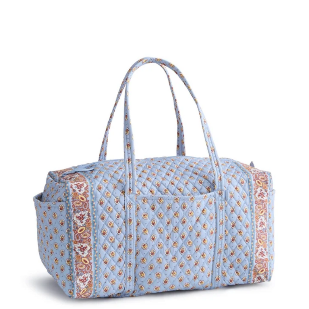 A light blue quilted duffel bag with a repeating paisley pattern in orange, pink, and white, featuring dual top handles and side pockets, shown on a white background.