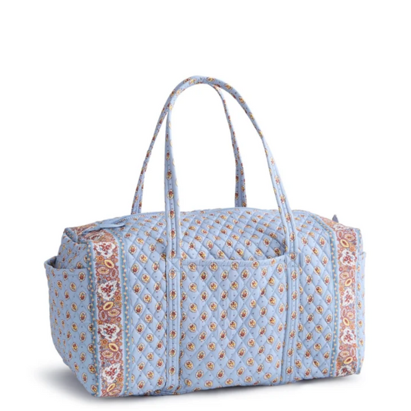 A light blue quilted duffel bag with a repeating paisley pattern in orange, pink, and white, featuring dual top handles and side pockets, shown on a white background.