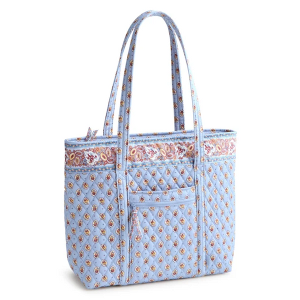 A light blue quilted tote bag with a repeating floral pattern, featuring a front pocket and a decorative floral border trim near the top, shown on a plain white background.