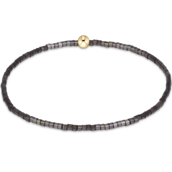 A beaded stretch bracelet made of small dark gray and black square beads with a single gold-toned round bead at the closure, shown on a plain white background.