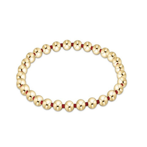Gold beaded bracelet with red accents on a white background