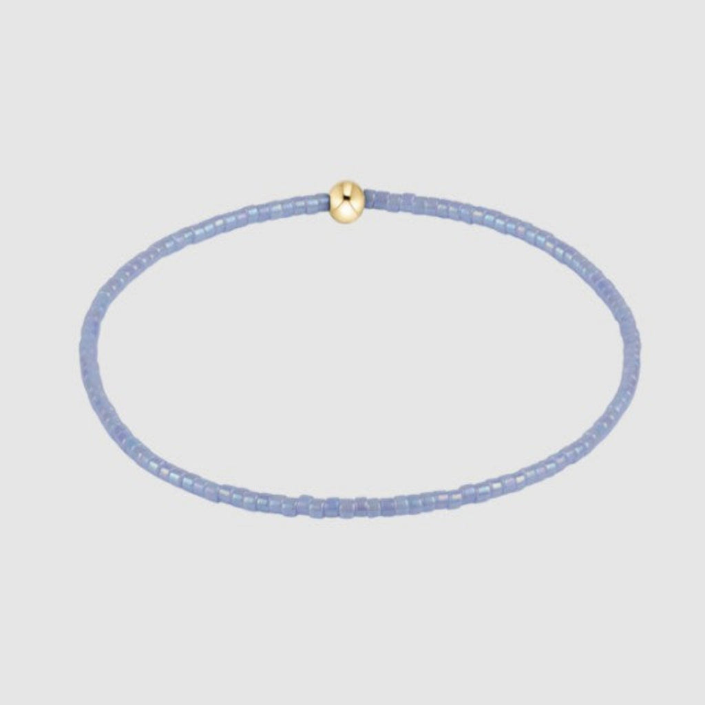 Thin blue beaded bracelee with a gold clasp on a light gray background