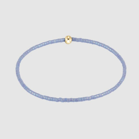 Thin blue beaded bracelee with a gold clasp on a light gray background