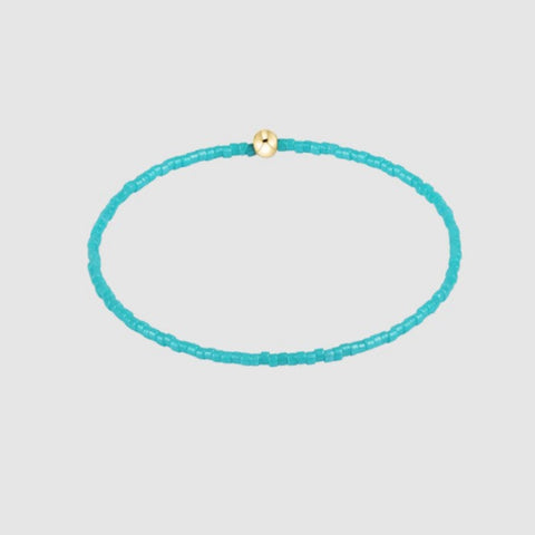 Turquoise beaded bracelet with a gold clasp on a light gray background