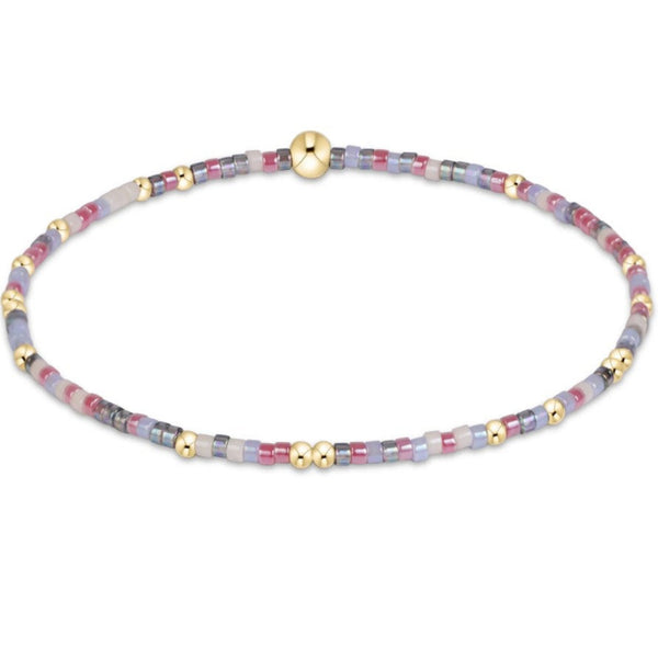 A delicate beaded stretch bracelet with small cylindrical beads in pastel lavender, pink, gray, and white, accented with gold spacer beads and a polished gold magnetic clasp, shown on a plain white background.