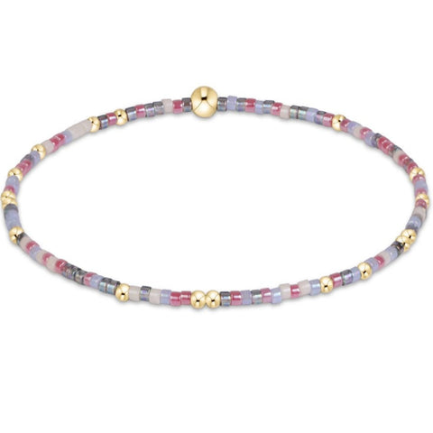 A delicate beaded stretch bracelet with small cylindrical beads in pastel lavender, pink, gray, and white, accented with gold spacer beads and a polished gold magnetic clasp, shown on a plain white background.