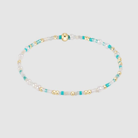 Beaded necklace with white, turquoise, and gold beads on a light gray background