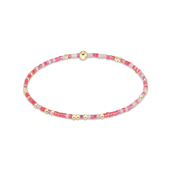 A delicate beaded bracelet with pink and white beads, accented by small gold spacer beads and a central gold bead, displayed on a clean white background.