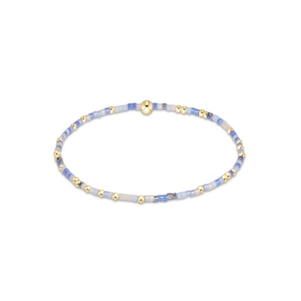A delicate beaded stretch bracelet featuring pale blue and white beads with small gold spacer beads and a gold magnetic clasp, shown on a plain white background.