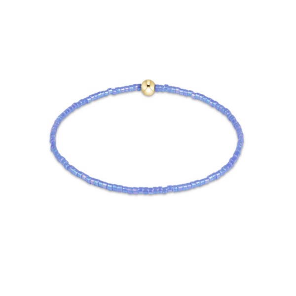 A delicate beaded bracelet featuring small, faceted light blue beads and a single central gold-toned bead with a tiny black accent, displayed on a clean white background.