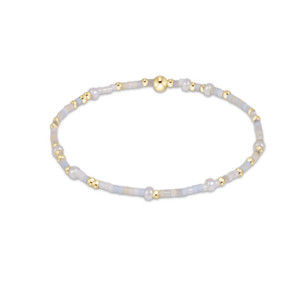 A delicate beaded stretch bracelet featuring pale gray and white beads with small gold spacer beads and a gold magnetic clasp, shown on a plain white background.