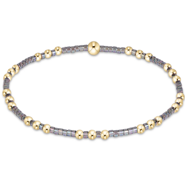 A beaded stretch bracelet featuring alternating metallic gold round beads and iridescent gray-blue square beads, with a larger polished gold bead at the top center, shown on a plain white background.