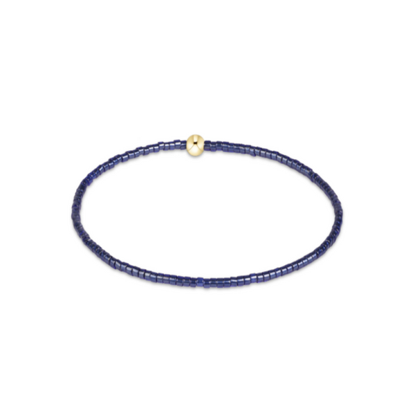 A delicate beaded bracelet composed of small dark blue beads with a single polished gold clasp, displayed on a clean white background.