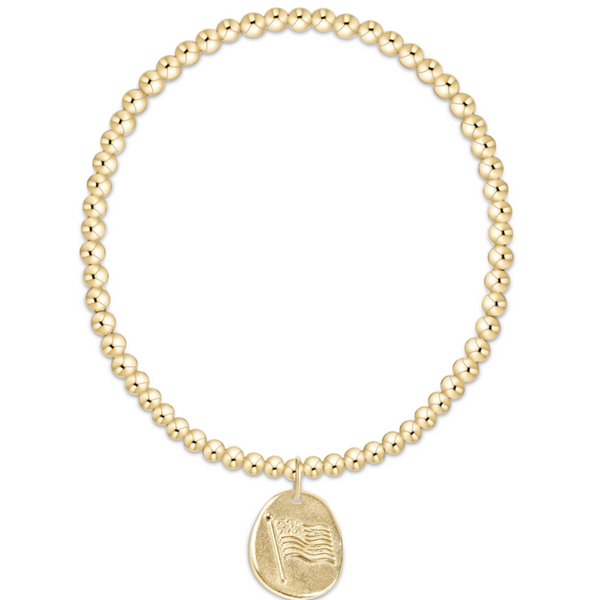 A gold beaded bracelet with a small oval pendant featuring an engraved American flag design, shown on a plain white background.