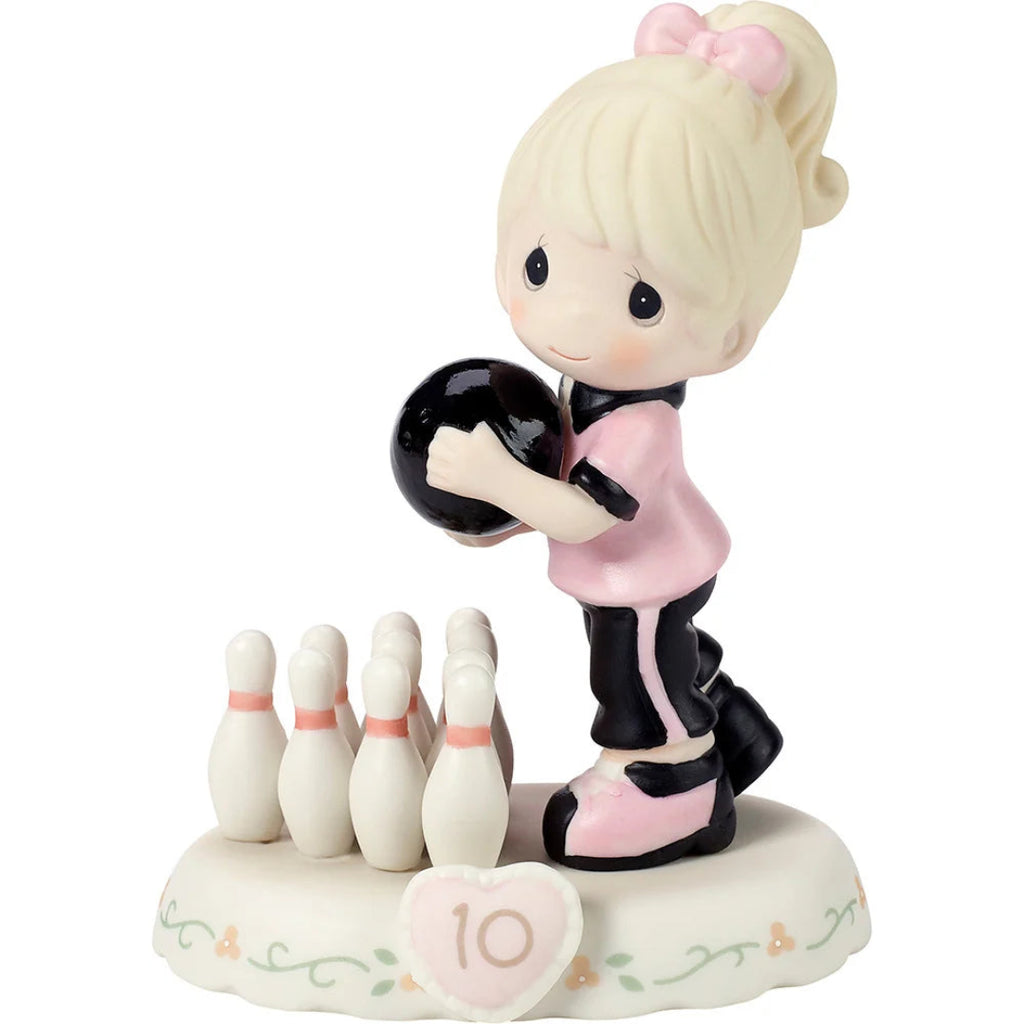 A Precious Moments style ceramic figurine of a young girl bowling, holding a black bowling ball and standing beside a set of white bowling pins on a decorative base with a pink heart-shaped number 10.