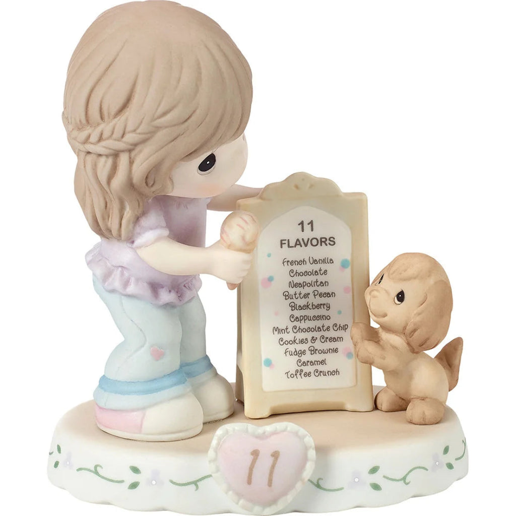 A Precious Moments figurine depicting a girl holding a sign with 11 flavors next to a small dog, on a white background.