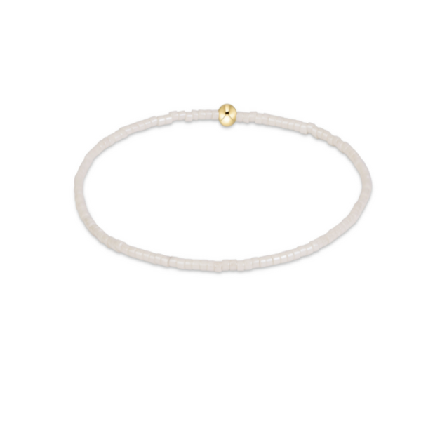 A delicate beaded bracelet made of small off white beads with a single small gold bead accent at the top, shown on a plain white background.